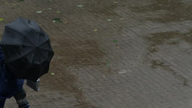 a man in a blue raincoat and with a black umbrella walks down the street in the rain