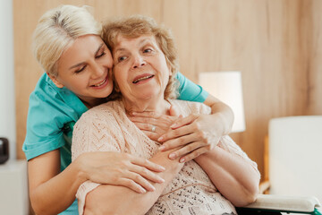 Young, smiling nurse hugging elderly woman in wheelchair