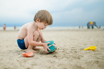 Cute little boy having fun on a sandy beach on warm and sunny summer day. Kid playing by the ocean. Summer activities for children