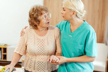 Smiling nurse assisting elderly woman using walking frame, rehabilitation concept