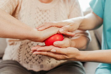 Nurse assisting elderly patient with hand physical therapy using red stress ball closeup, selective focus