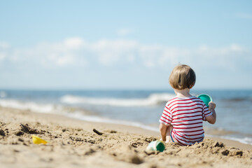 Cute little boy having fun on a sandy beach on warm and sunny summer day. Kid playing by the ocean. Summer activities for children