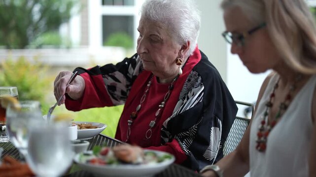 Closeup focus shift from mature woman to elderly woman as they eat at outdoor cafe.