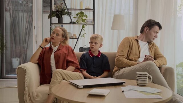 Medium long shot of teenage son sitting between his parents having argue in living room at home
