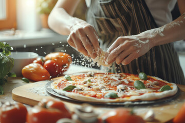 A close-up view of someone in an apron spreading cheese over a freshly made pizza, with fresh ingredients scattered around on a rustic kitchen counter.
