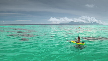 Woman is paddling on her sup board in a turquoise lagoon, enjoying a sunny day. She is exercising in a wonderful exotic location