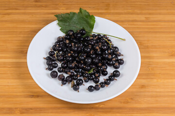 Ripe fresh blackcurrant with leaf on dish on wooden surface