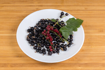 Ripe fresh redcurrant and blackcurrant on dish on wooden surface