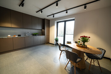 Interior of a Modern furnished Kitchen in a New House. Dining Table and Chairs in Stylish and Functional Space. Detailed kitchen Design. Dining table with plates, glasses and vase of red roses.