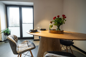 Interior of a Modern furnished Kitchen in a New House. Dining Table and Chairs in Stylish and Functional Space. Detailed kitchen Design. Dining table with plates, glasses and vase of red roses.