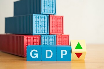 Wooden blocks GDP, arrow triangle up and down with heap shipping container background. GDP (Gross Domestic Product) growth or decline in economic crisis, global world trading, business and economy.