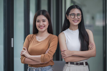 Happy two Asian businesswomen standing with arms crossed looking at the camera in the office.