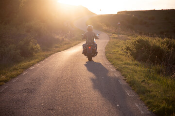 Biker driving a motorcycle rides along the asphalt road in sunset.