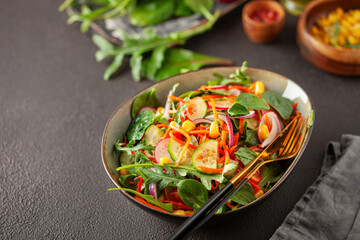 Fresh salad with vegetables. Arugula, spinach, cucumbers, tomato, onions carrots, corn andradishes in a plate on the table. Diet nutrition.  Copy space