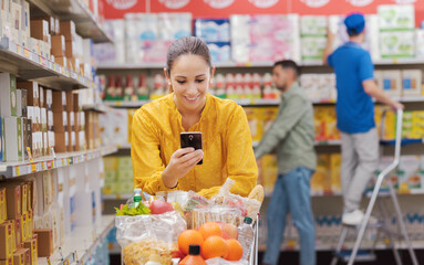 Fototapeta premium Woman buying groceries at the supermarket and connecting with her smartphone