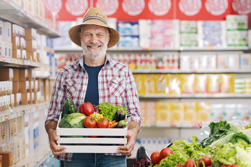 Happy farmer holding a crate full of vegetables at the grocery store