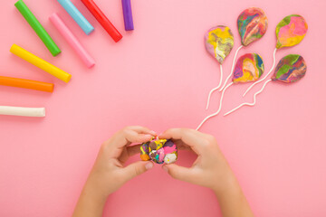 Baby girl hands kneading and creating colorful balloon from modeling clay on pastel pink table background. Closeup. Point of view shot. Toddler development. Little child making shapes. Top down view.