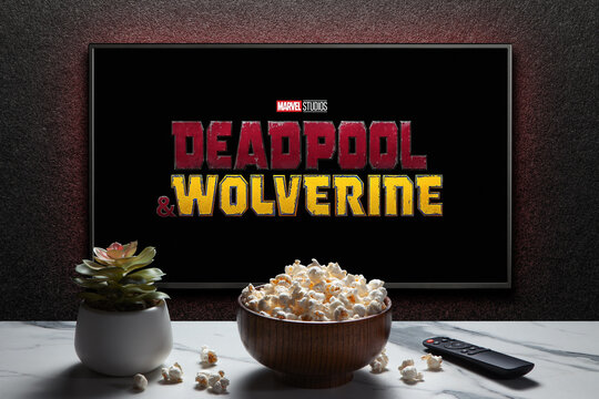 Wolverine and Deadpool trailer or movie on TV screen. TV with remote control, popcorn bowl and home plant. Astana, Kazakhstan - July 31, 2024.