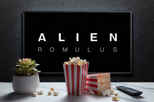Alien Romulus trailer or movie on TV screen. TV with remote control, popcorn boxes and home plant. Astana, Kazakhstan - July 31, 2024.