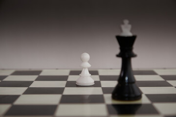 Black chess king and a white pawn on a chessboard close-up, pawn and king, chess pieces on a chessboard, opposite chess pieces, underdog; underdog story;