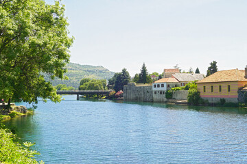 Fototapeta premium Summer landscape from the center of Trebinje: the Trebišnjica River, trees, houses of the Old Town on the bank and a mountain in the distance. Tourist places in Bosnia and Herzegovina.