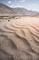Sandy desert with dunes in Tien Shan mountains on Pamir Highway in Tajikistan against the backdrop of mountain rocky peaks and Panj River in Wakhan Valley, mountain landscape for background