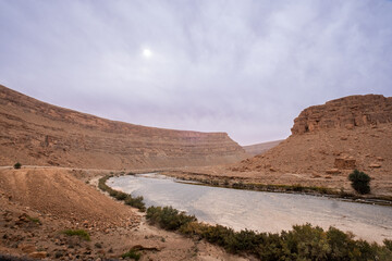 A dry river runs through the canyon between the Middle Atlas Mountains towards the Moroccan desert. Landscape similar Mars or the Colorado Canyon. A herd of goats crosses the riverbed in the distance
