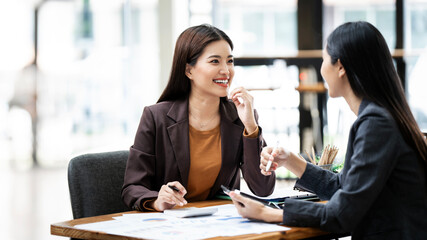 Two happy busy asian female employees working together using computer planning project.