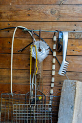 A rustic wooden wall displays a collection of hanging tools, including a garden rake, a wire...