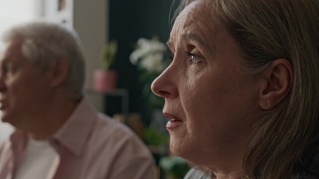 Medium closeup with slowmo of sad mature Caucasian woman looking at her husband indifferently while visiting family psychologist at modern office