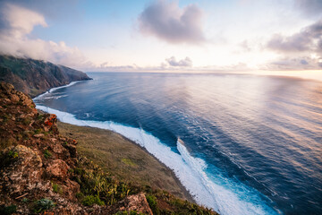 View of rough ocean with waves, volcanic beach, sunset over a huge cliff  in Lighthouse Ponta do Pargo, Madeira, Portugal