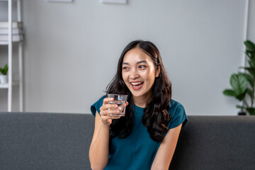 A woman is sitting on a couch and smiling while holding a glass of water