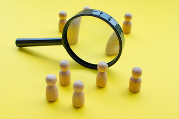 Magnifying glass surrounded by wooden figures. This can represent searching for job, or group...