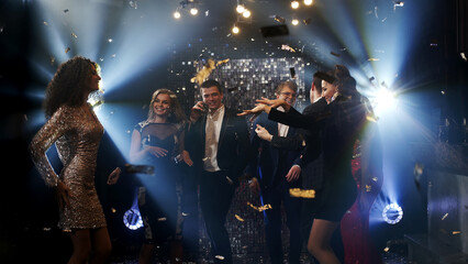 Young adults dancing at a disco on a weekend evening, illuminated by colorful light effects. A...