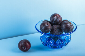Ripe plums in a blue antique glass vase on a blue background.