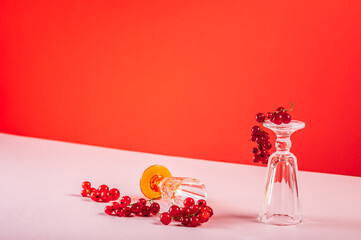 Two glass goblets with red currants, still life with red berries on a red background.