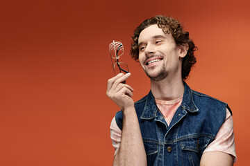 A charming man enjoys a moment, smiling and holding glasses against a bright background.