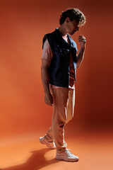 A stylish man poses thoughtfully on a warm, colorful backdrop.