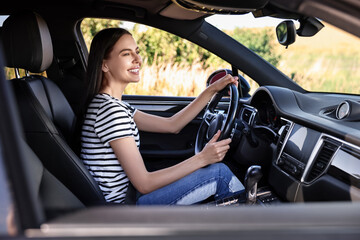 Naklejka premium Smiling young woman holding steering wheel while driving car, view from outside