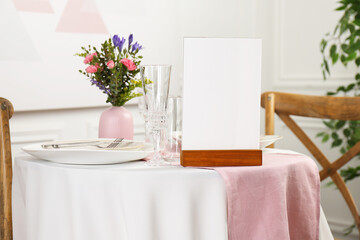 Menu holder, clean dishware and vase with beautiful flowers on white table in restaurant