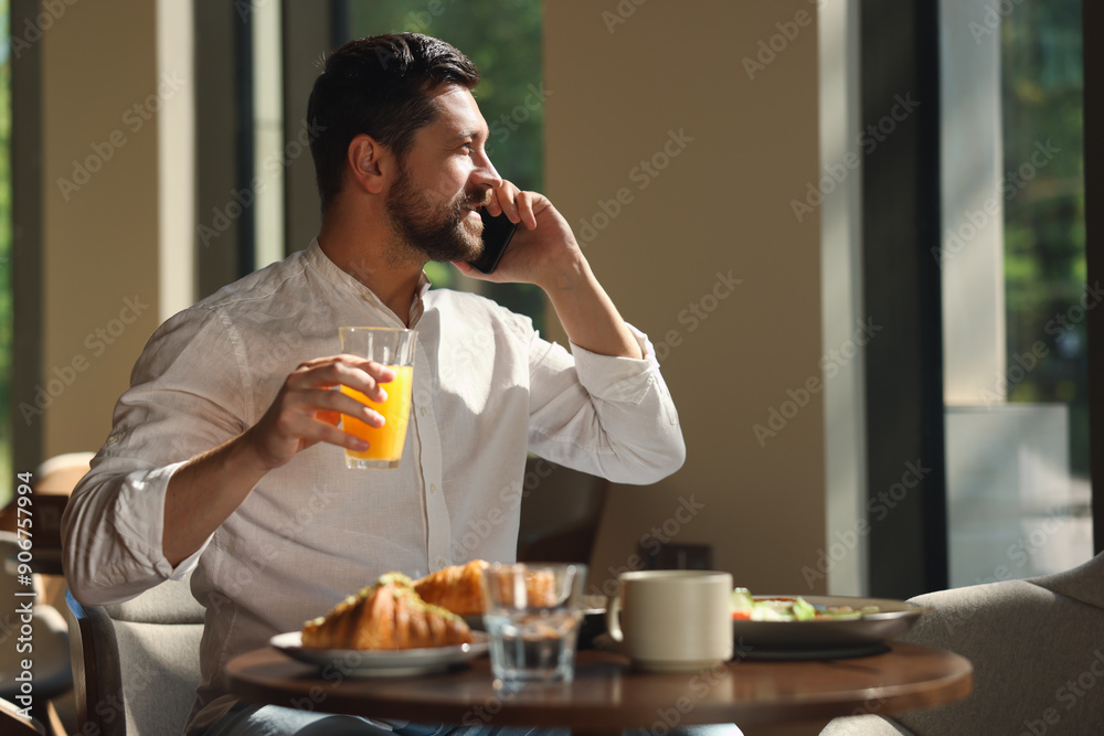 Canvas Prints Happy man having tasty breakfast while talking on smartphone in cafe, space for text