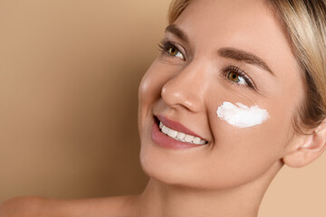 Beautiful woman with cream on her face against beige background, closeup. Space for text