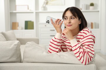 Beautiful woman with smartphone listening to voice message at home