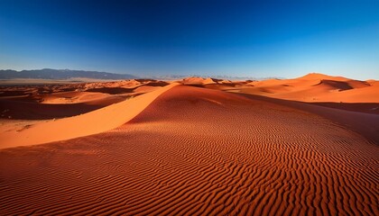 A vast desert landscape with dramatic red sand dunes under a clear, deep blue sky, showcasing the intricate patterns formed by the wind.

