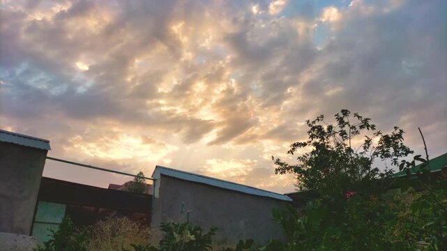 Time lapse of movement of clouds across sky at sunset with change in color, illumination of sky. Wide-angle view with geometric distortions of verticals, buildings and structures for vertigo effect