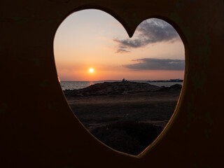 View through the fence hole in the shape of heart. Man sitting thoughtfully at the seashore and...