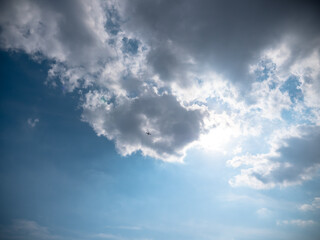 Airplane flying high up in the sky below dark blue stormy clouds with sun shining through them.