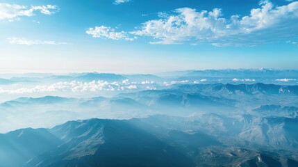 A breathtaking aerial view of mountain ranges under a clear blue sky with scattered clouds, showcasing the beauty of nature and tranquility.
