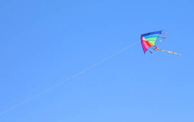 colorful kite with rainbow colors flying in the sky tied to a string
