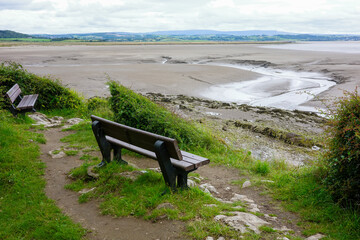 Empty benches overlooking a vast, serene tidal flat with distant hills and a cloudy sky. Jenny Browns Point Silverdale Lancashire UK.